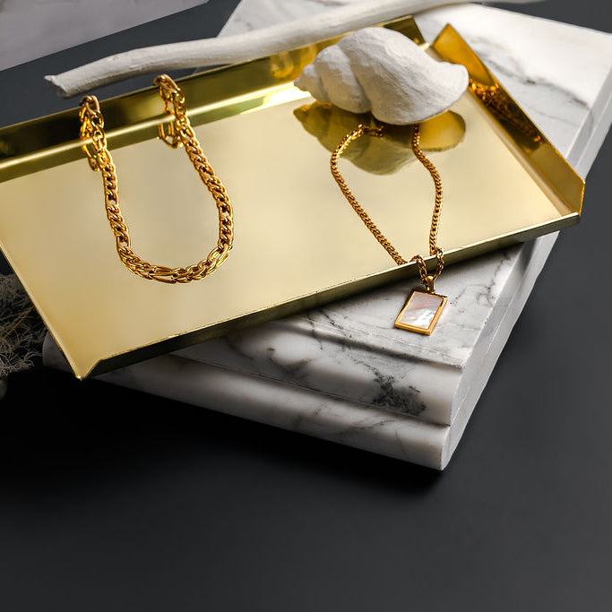 A polished brass tray, shaped as a rectangle sitting atop a marble slab.