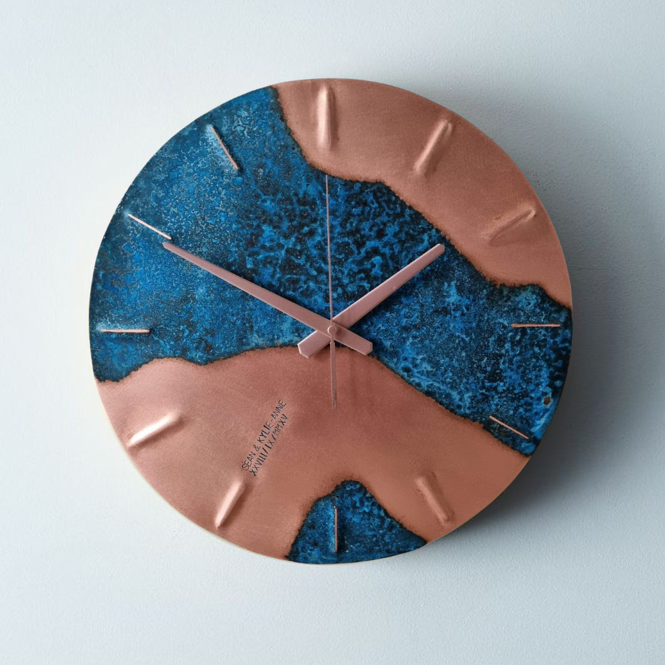 A round, blue patina, copper “half time” wall clock made by Empire Copper on a light grey background.